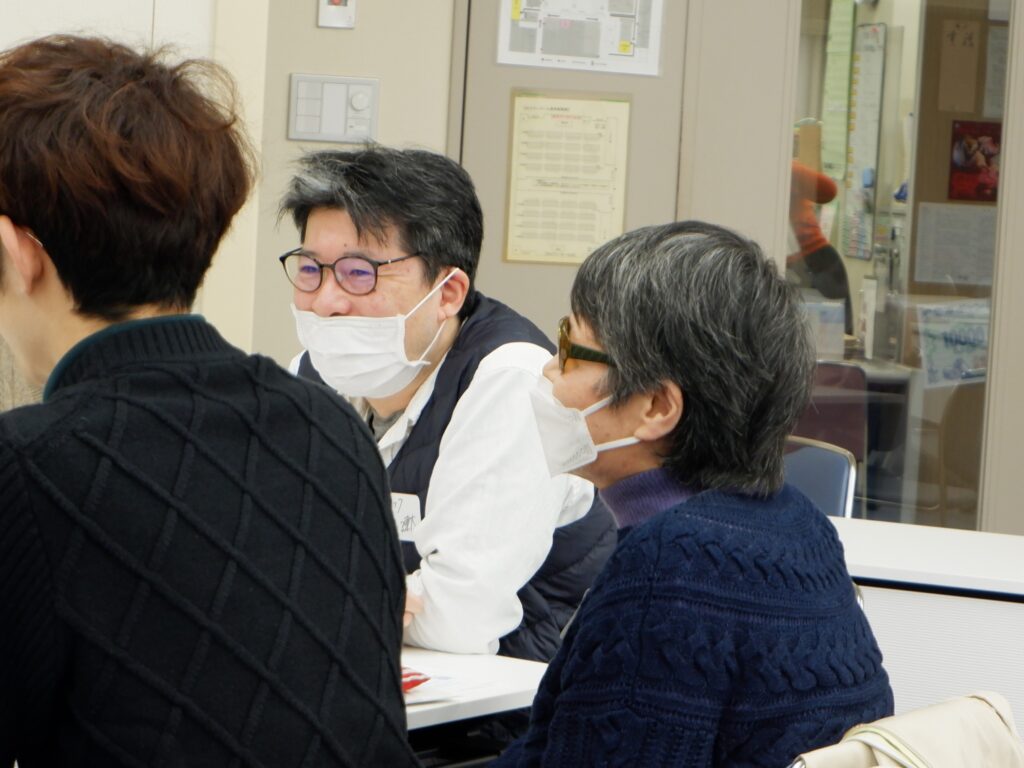 テーブルについてワークショップをしている。佐藤さんの左横顔とほほ笑む林の斜め左横顔が写っている。